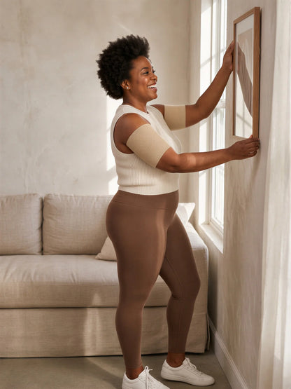 A woman in her late thirties hanging a picture, wearing beige arm sleeves