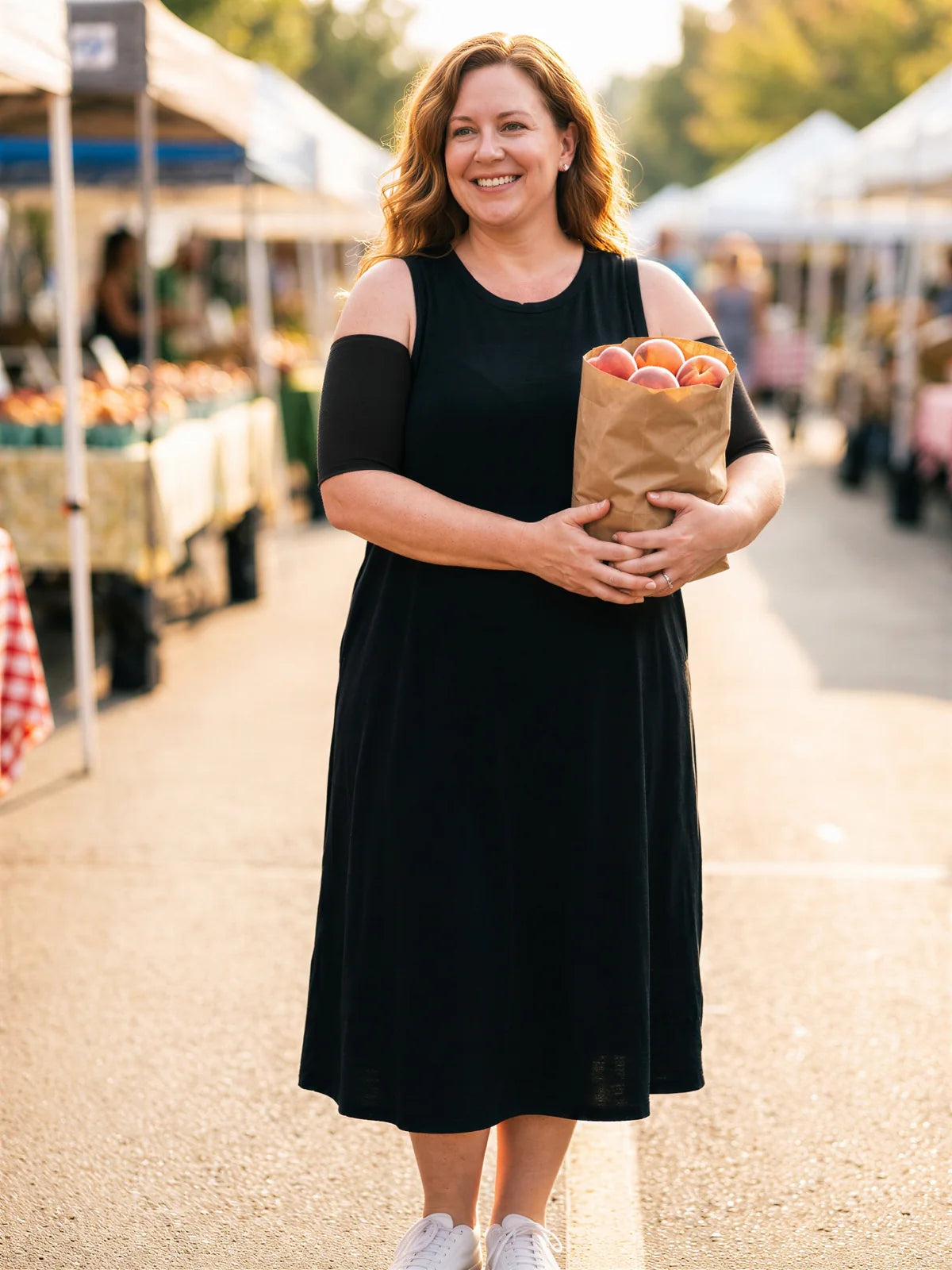 A woman at a farmers' market wearing black arm sleeves under a sleeveless dress