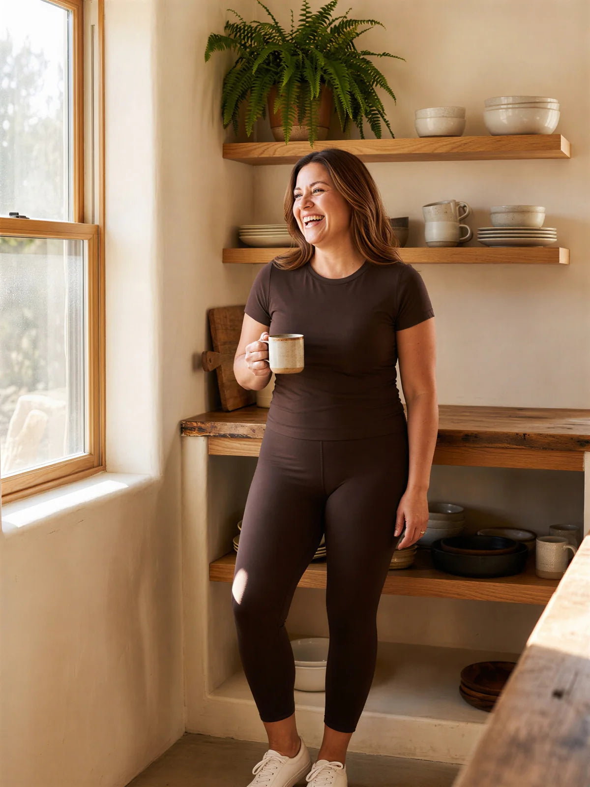 A woman in her forties laughing in her kitchen in the coffee top