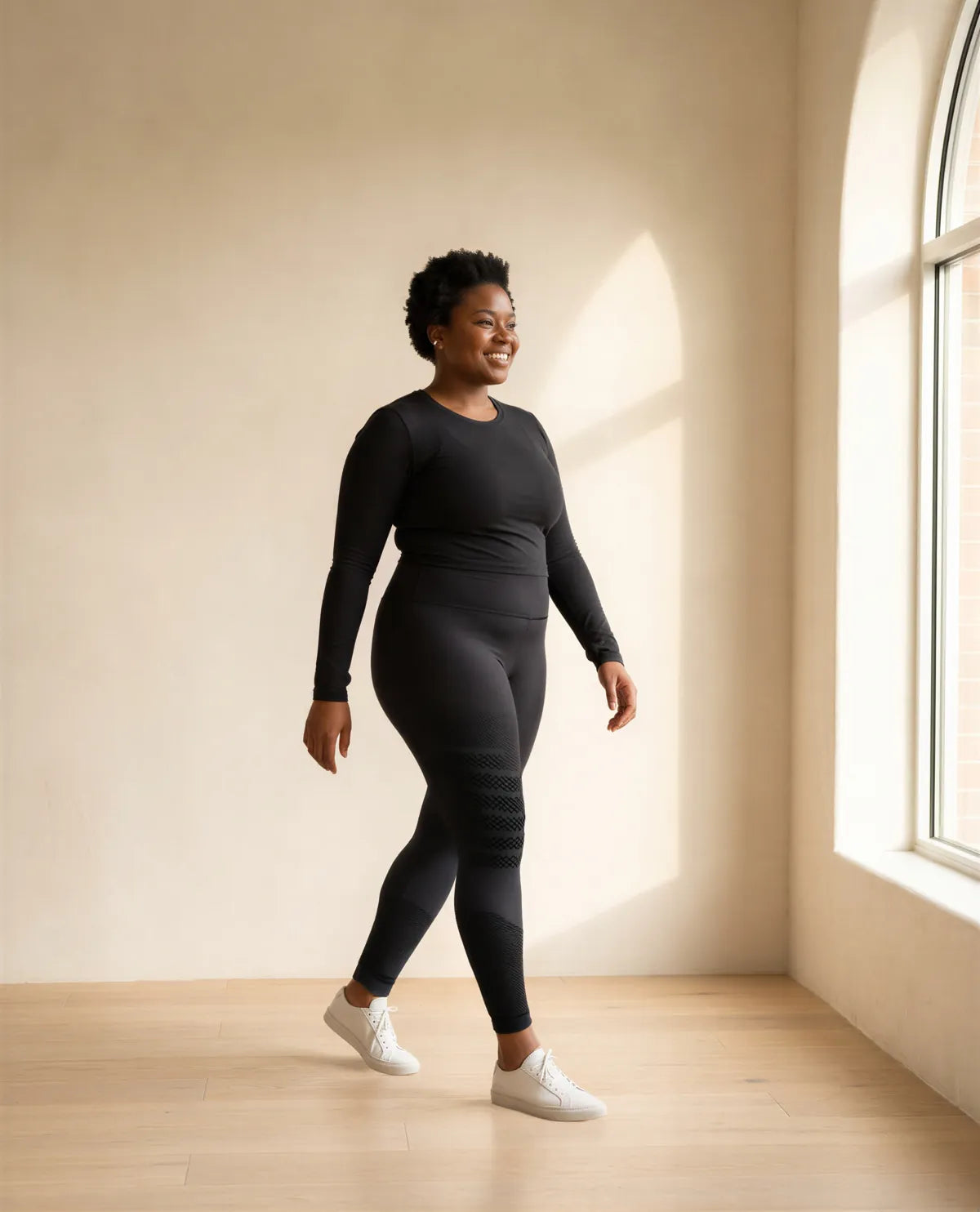 A woman walking across a sunlit studio in black leggings