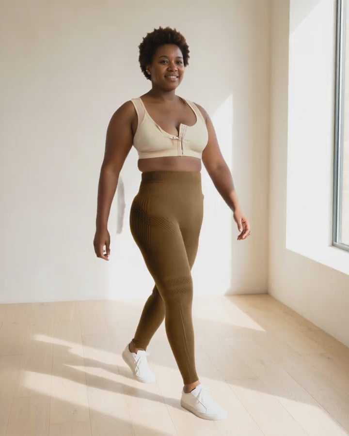 A woman walking slowly to the window in the beige bra and coffee leggings