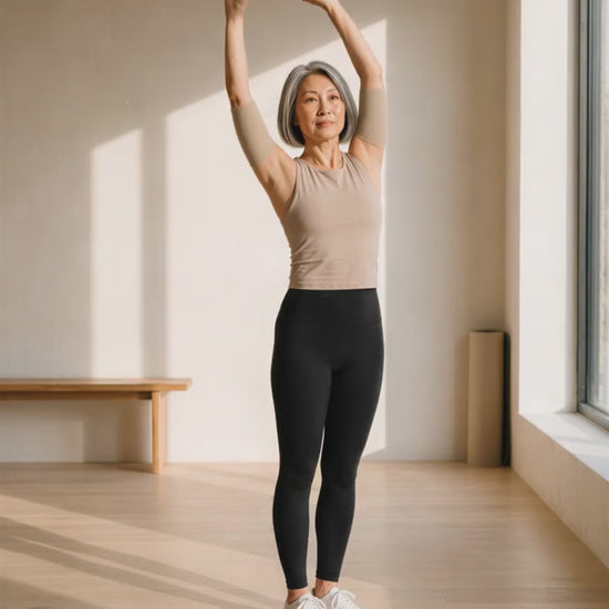 A woman in her fifties lowering her arms after a stretch, wearing beige arm sleeves