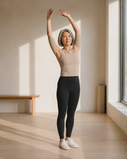 A woman in her fifties lowering her arms after a stretch, wearing beige arm sleeves